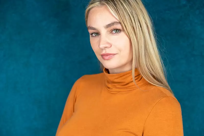Actor headshot of a woman in an orange turtleneck on a dark background