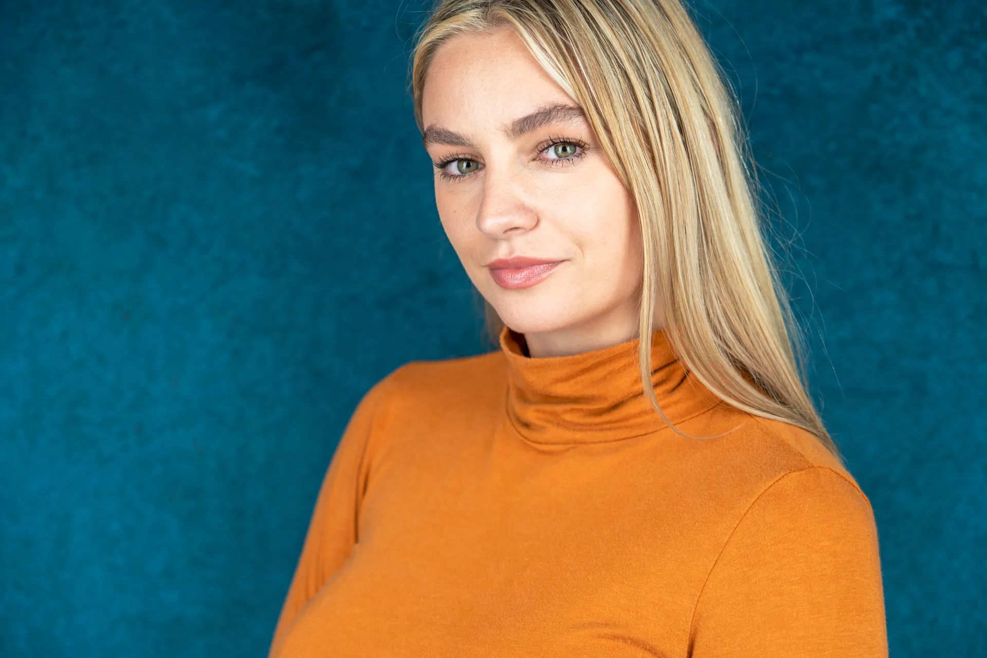 Actor headshot of a woman in an orange turtleneck on a dark background