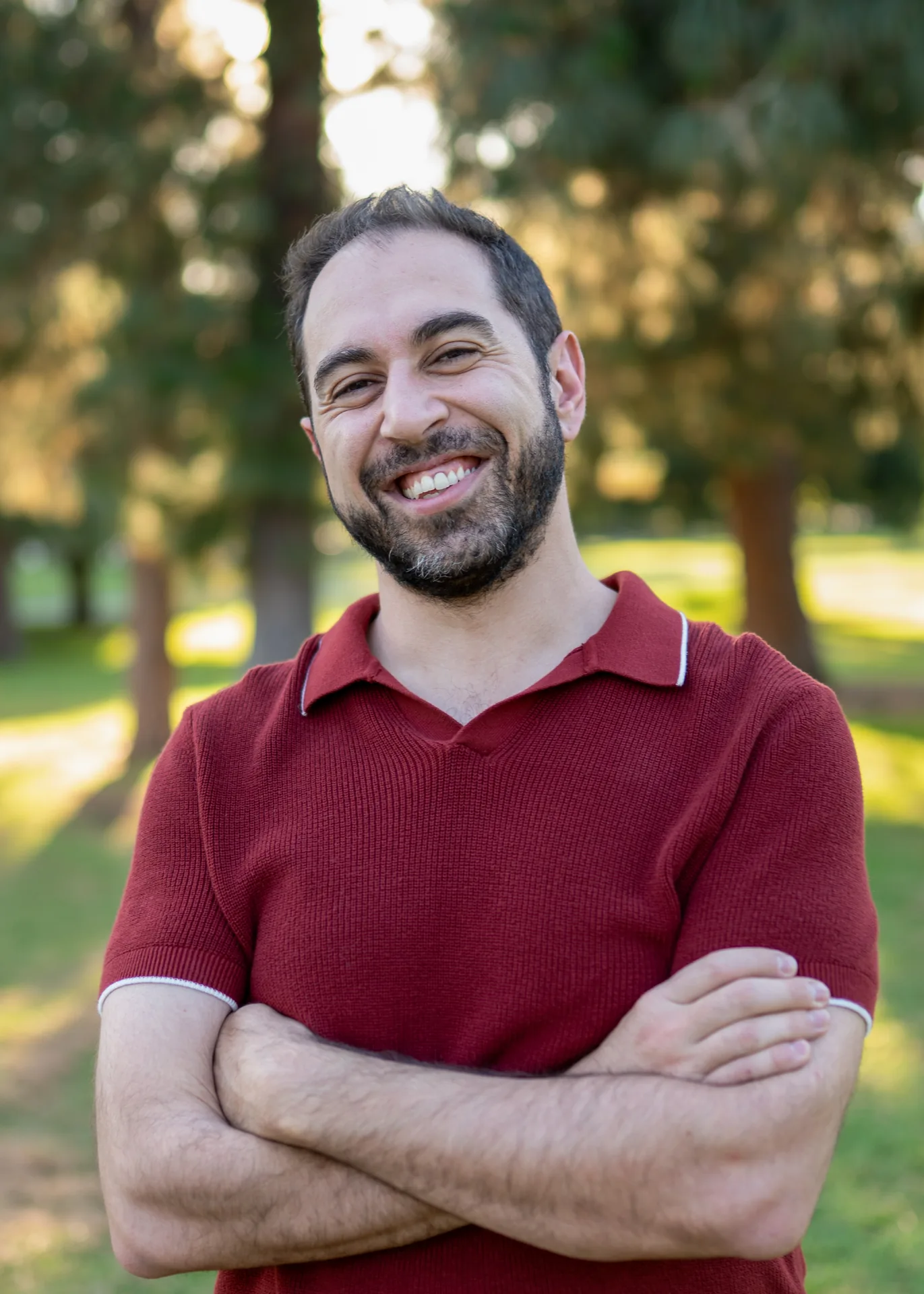 Outdoor headshot of a bearded man in a red shirt, photographed in a park